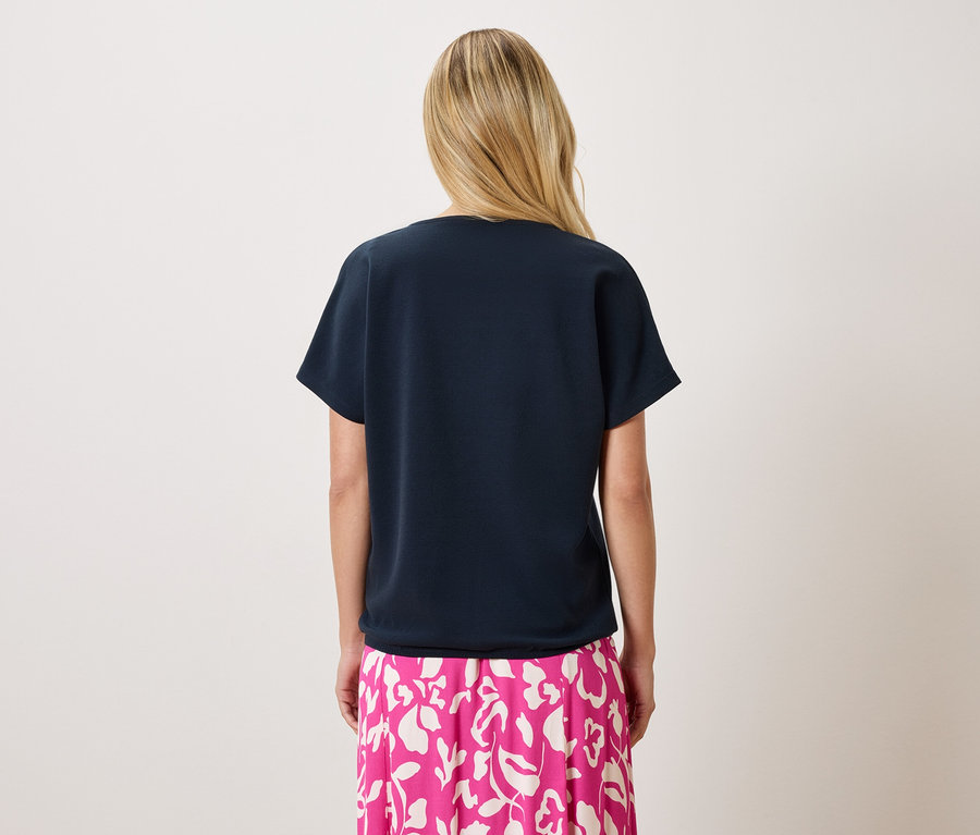 Vue de dos d'une femme blonde portant un t-shirt bleu marine et une jupe rose à imprimé floral.