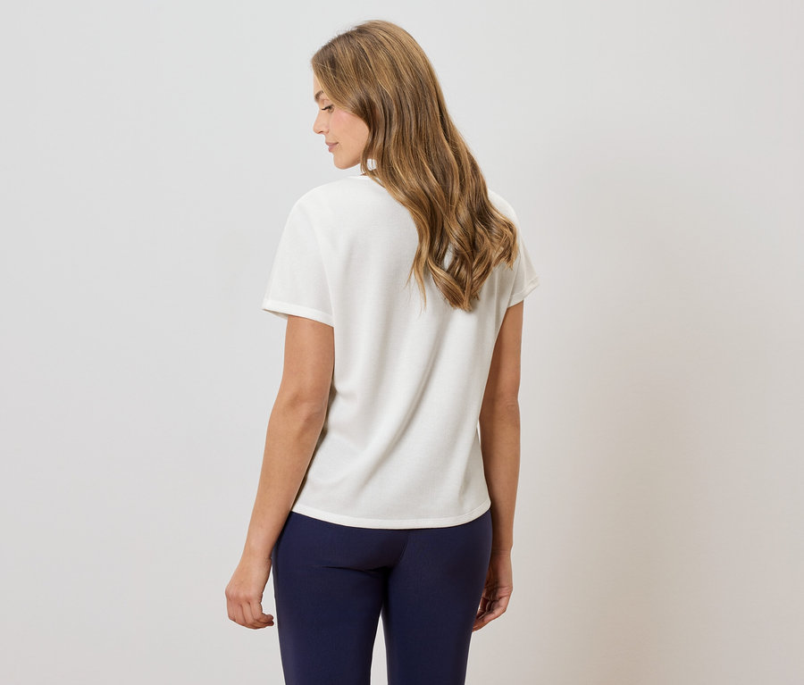 Vue de dos d'une femme aux cheveux ondulés mi-longs portant un t-shirt crème et des leggings bleu marine.