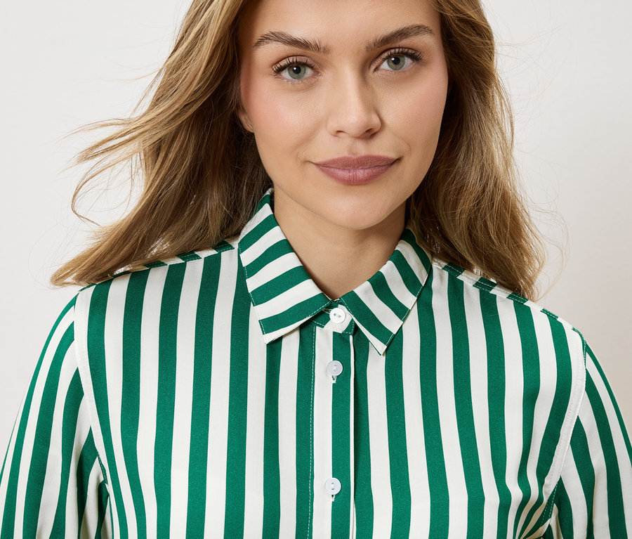 Portrait d'une femme aux cheveux blonds ondulés portant une chemise rayée vert émeraude et blanc.