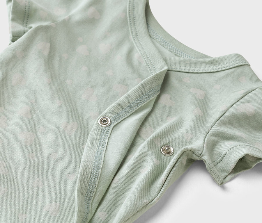 Gros plan sur un body de bébé vert clair avec un motif de petits cœurs blancs et des boutons-pression.
