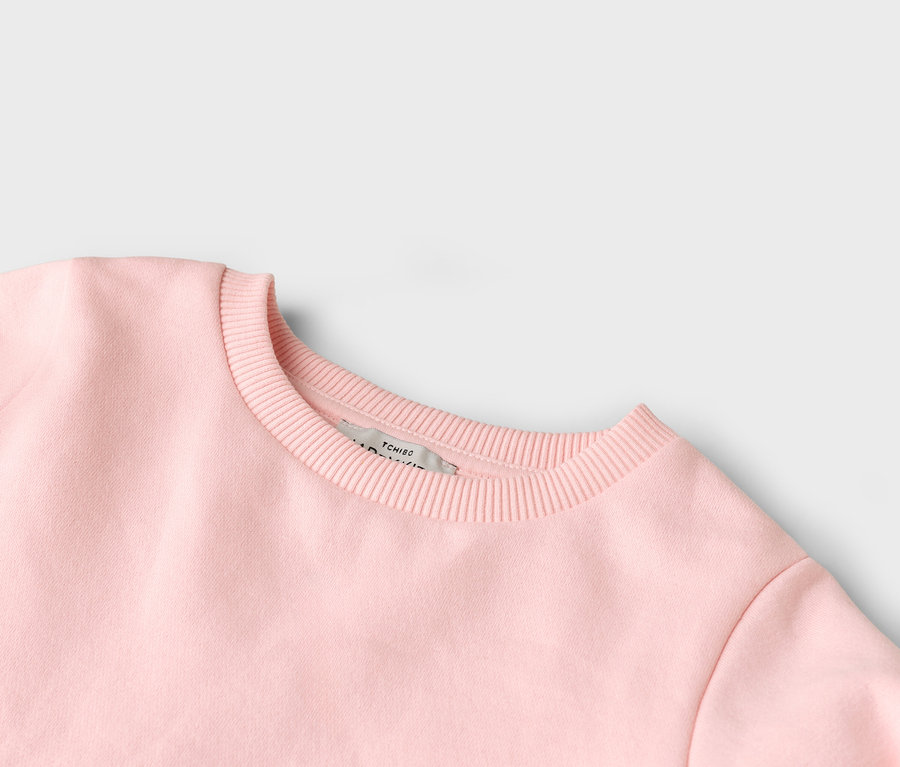 Gros plan d'un pull rose à col rond avec une étiquette Tchibo.