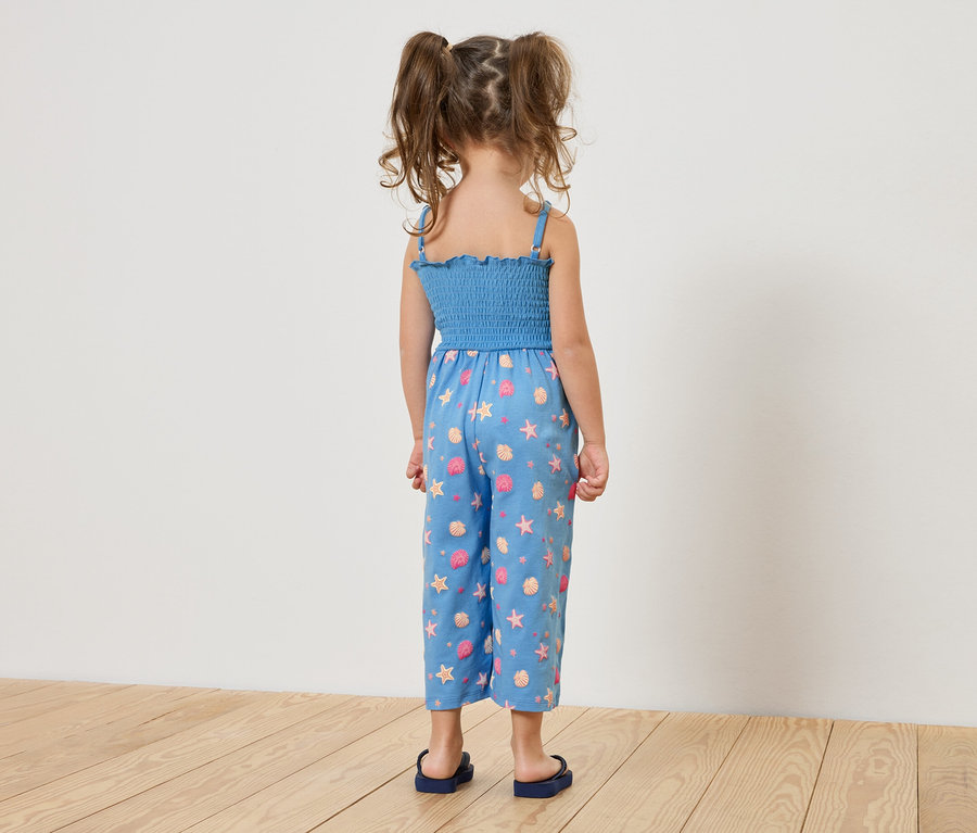 Vue arrière d'une petite fille avec des tresses, portant une combinaison bleue avec un motif d'animaux marins et des sandales bleues.