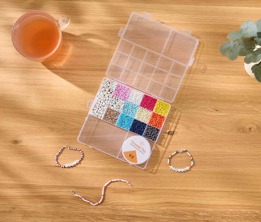 Sur une table en bois se trouvent une tasse, une boîte de perles, une bobine Crystal Tec et trois bracelets de perles.