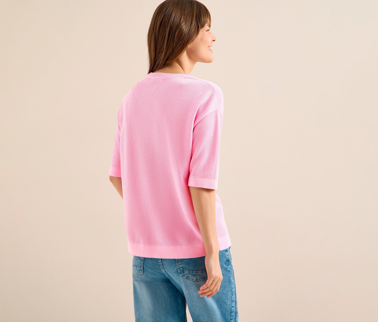Femme de dos portant un pull à manches courtes CECIL rose et un jean.