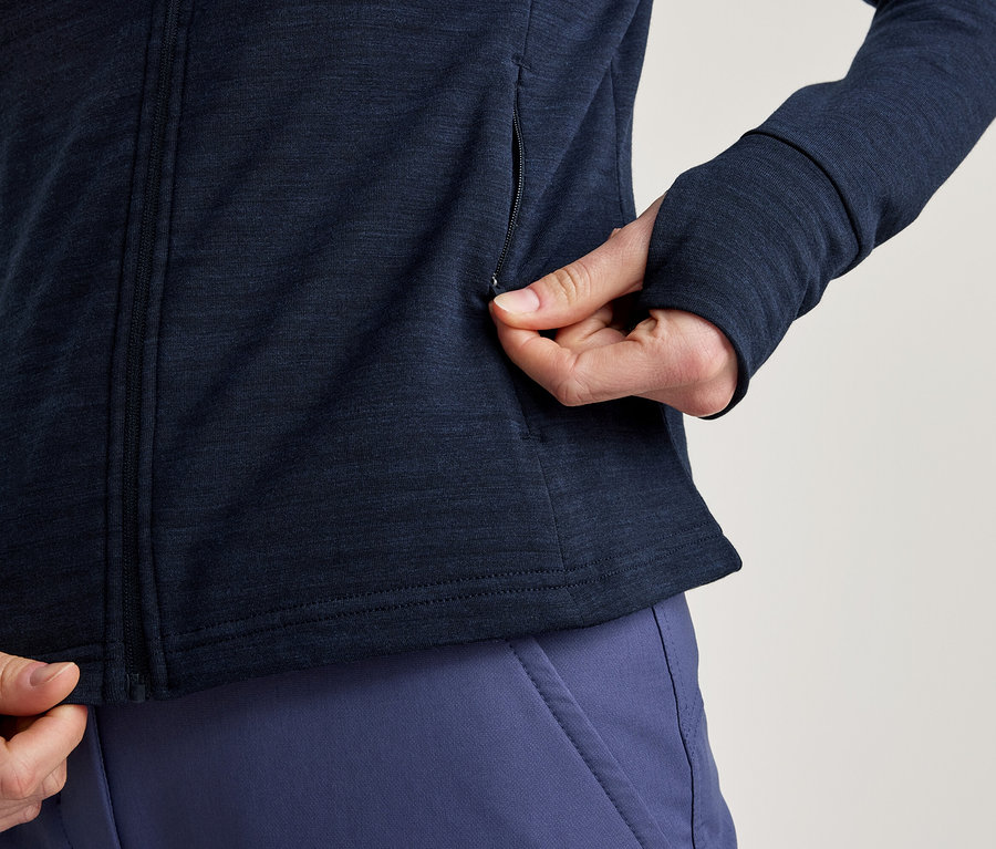 Personne portant une veste bleu marine zippée avec des trous pour les pouces, ouvrant une poche latérale, avec un pantalon bleu.
