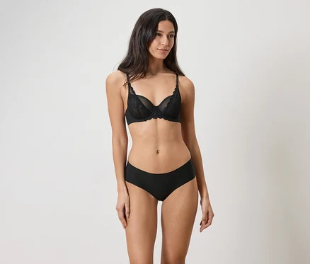 Une femme porte un soutien-gorge en dentelle noire et une culotte noire.