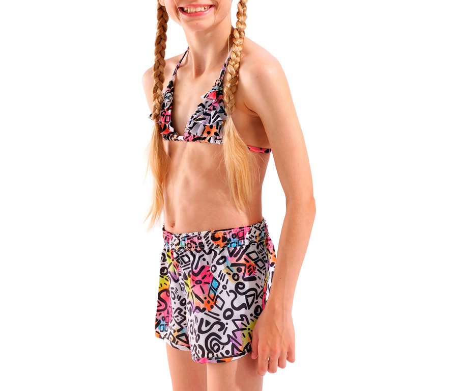 Une jeune fille aux cheveux blonds tressés porte un haut de bikini coloré et un short à motifs géométriques sur un fond blanc.