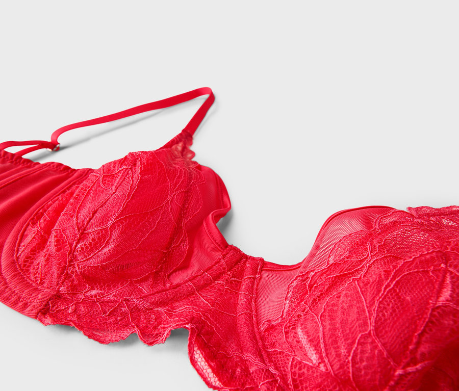 Gros plan d'un soutien-gorge rouge en dentelle avec bretelles réglables sur fond blanc.