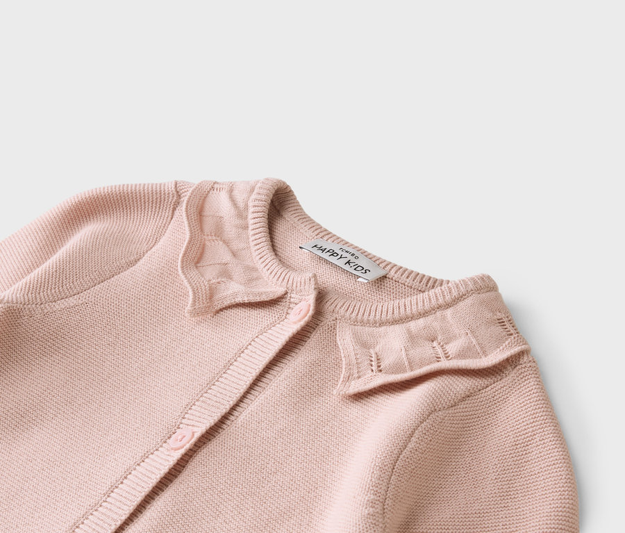 Gros plan sur un cardigan rose clair avec des boutons et une étiquette indiquant « ICHIBO HAPPY KIDS ».