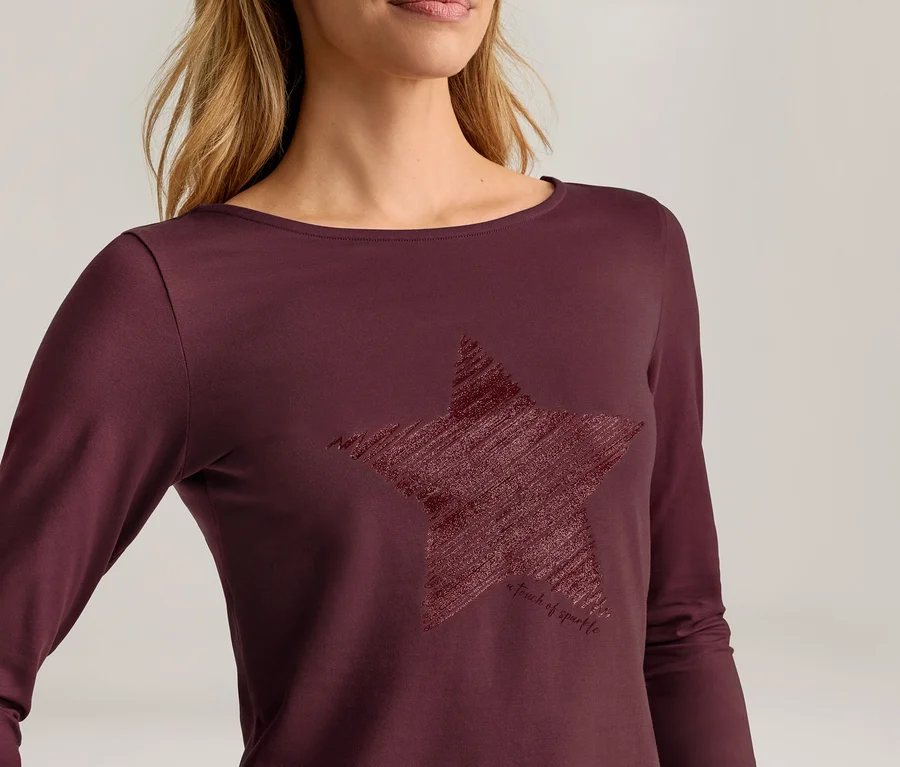 Femme portant un haut bordeaux à manches longues et col bateau, avec un grand motif d'étoile texturé et griffonné sur le devant.