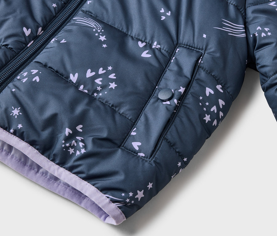 Gros plan d'une veste matelassée bleu marine zippée avec des détails violets, ornée d'étoiles, de cœurs et de comètes.