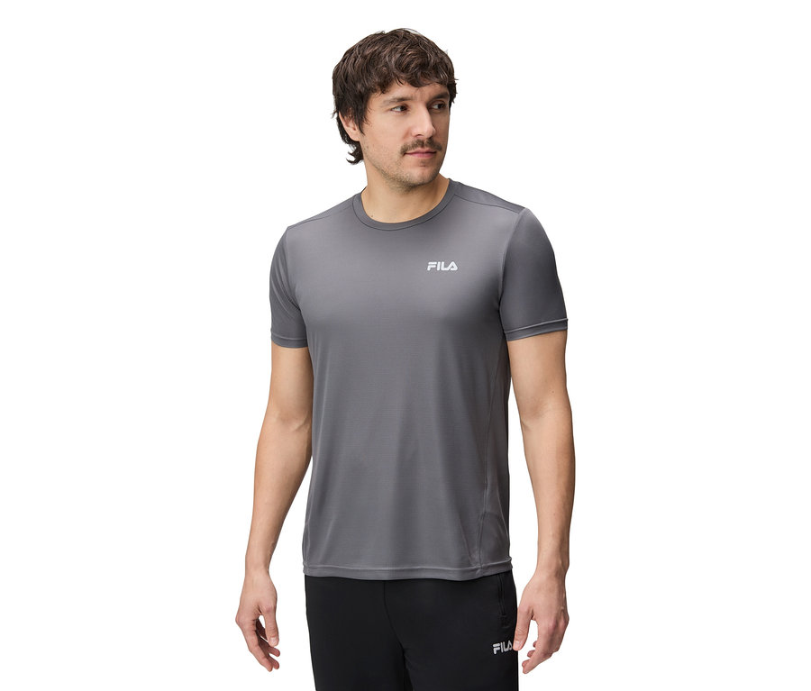Un homme porte un t-shirt Fila gris et un pantalon noir.