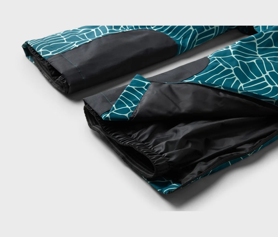 Gros plan sur deux jambes de pantalon à motif turquoise et blanc avec des sections noires, l'une partiellement ouverte pour montrer une doublure noire et un ourlet élastique.
