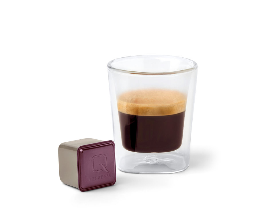 Une capsule Qbo Espresso ORO TOLIMA à côté d'une tasse à expresso.