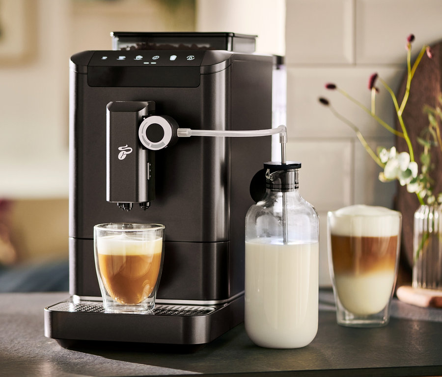Une machine à café entièrement automatique « Esperto 2 Milk » Granite Black prépare du café dans un verre. À côté se trouve une carafe à lait.