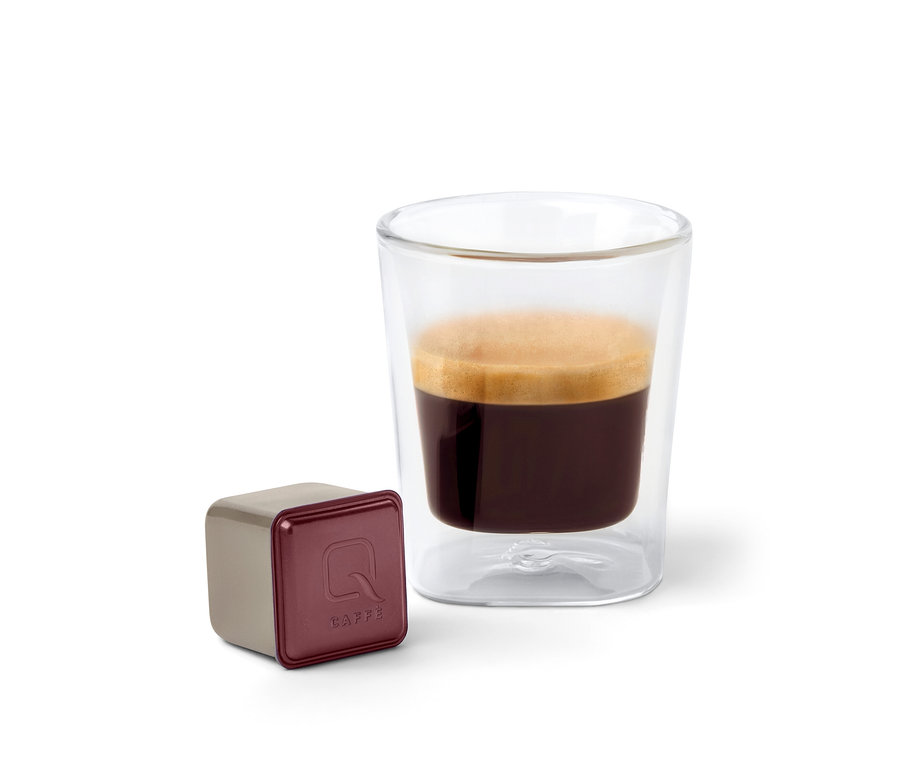 Une capsule Qbo Caffè KINYAA GALERAS est posée à côté d'un verre de café.