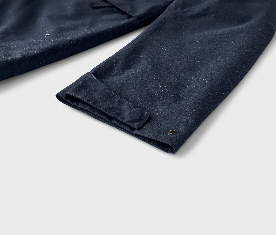 Gros plan d'une manche bleu foncé avec un poignet et un bouton-pression, parsemée de petites gouttelettes d'eau blanches.