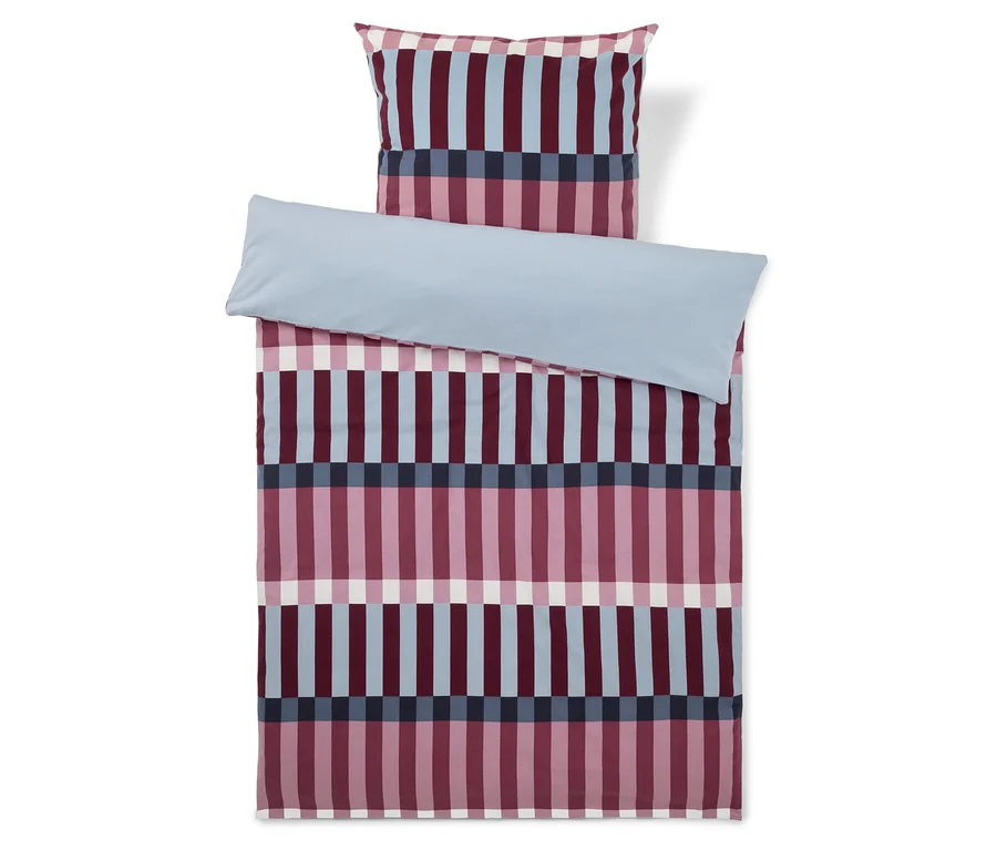 Parure de lit comprenant une taie d'oreiller et une housse de couette avec un motif à rayures verticales roses, bleu clair, bleu foncé et blanches. Un drap bleu clair est plié sur la partie supérieure de la housse de couette.