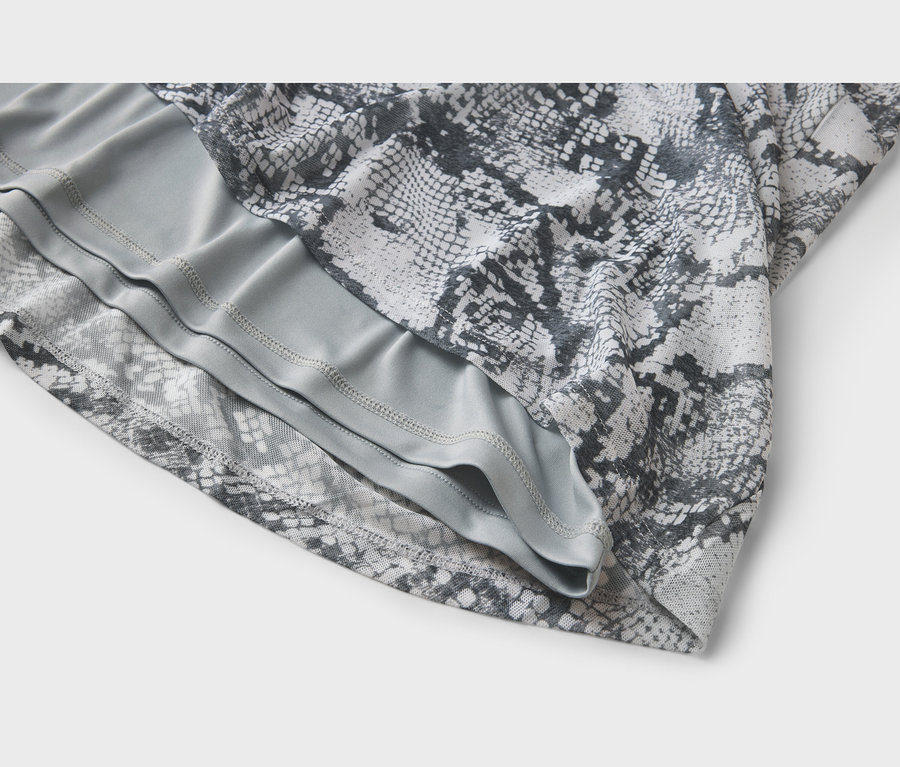 Gros plan sur un tissu superposé. La couche supérieure est blanche et grise avec un motif peau de serpent, révélant une sous-couche unie gris clair avec des coutures visibles.
