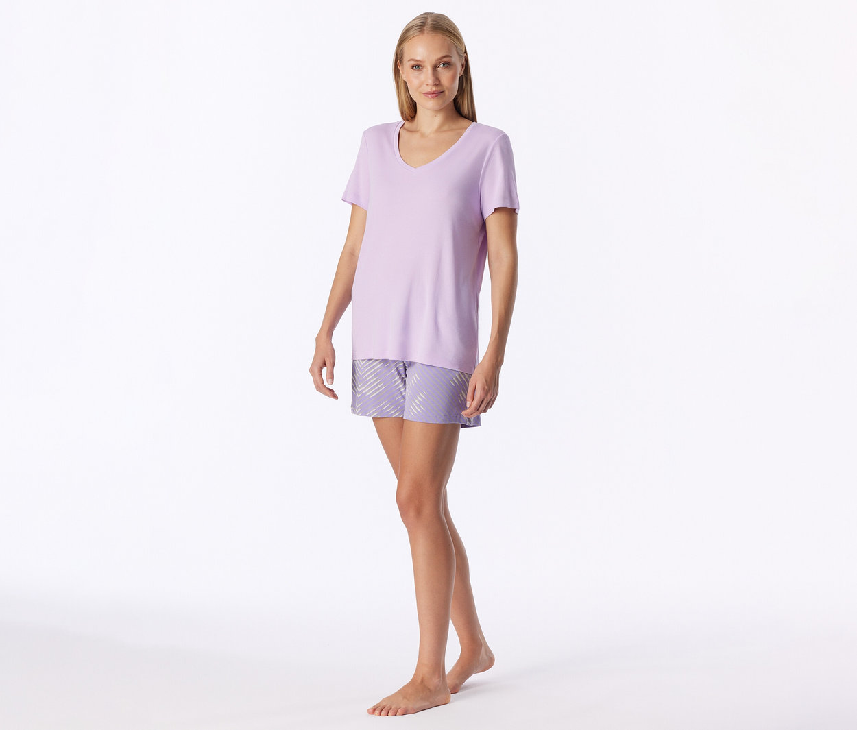 Femme debout portant un t-shirt lilas à col en V et un short à motifs à rayures diagonales, pieds nus.