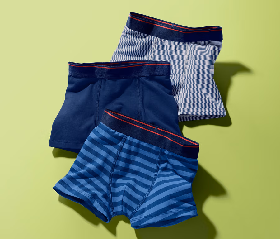 Trois boxers sur fond vert. Un bleu foncé, un bleu rayé et un gris rayé.
