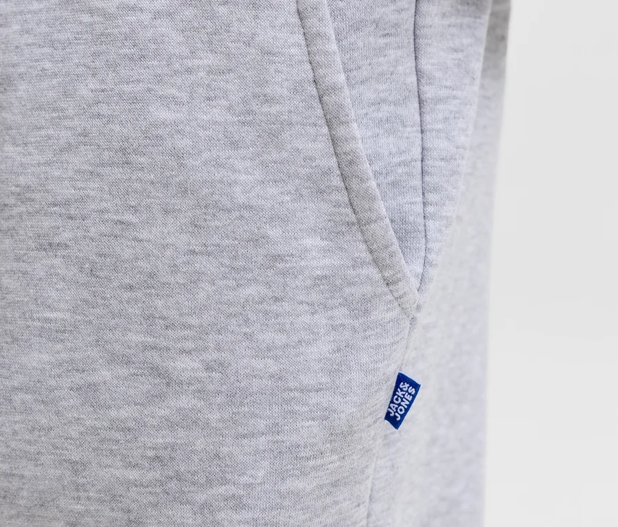 Gros plan d'un pantalon de survêtement gris Jack&Jones Bradley, montrant la texture du tissu, une poche latérale et une étiquette bleue Jack&Jones.