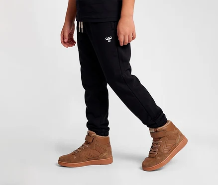 Personne portant un pantalon de jogging noir avec un logo hummel blanc et des baskets hummel® « St Power Play Mid Wt Jr » marron avec doublure en fourrure.