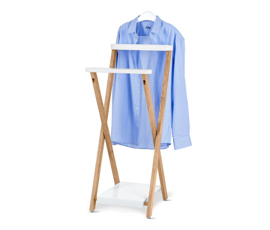 Une chemise bleu clair est suspendue à un cintre blanc sur un valet de chambre en bois avec des étagères blanches.