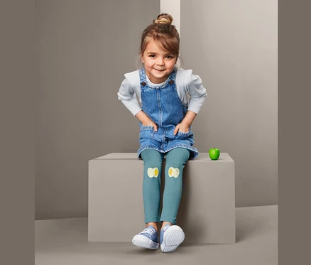 Une fille est assise et porte une robe en jean et 2 leggings avec des appliqués de poussins.
