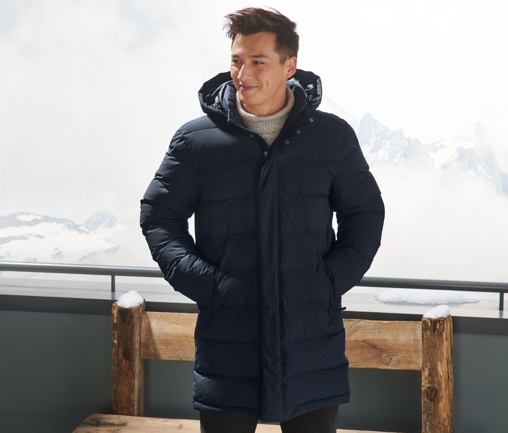 Un homme portant une parka matelassée en duvet bleu marine se tient à l'extérieur, les mains dans les poches.