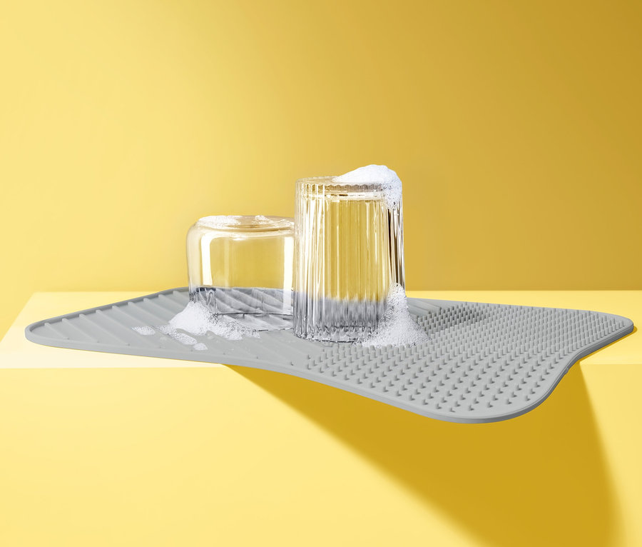 Verres avec du savon sur un tapis égouttoir à vaisselle en silicone gris.