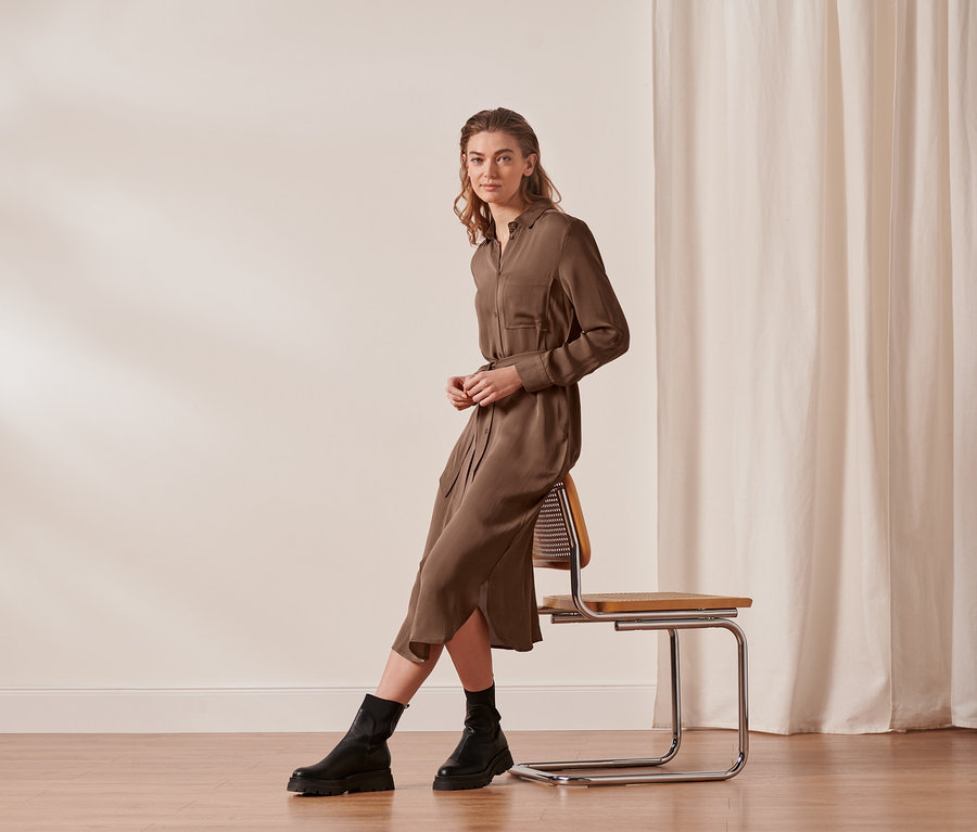 Une femme est assise sur une chaise et porte une robe-chemisier.