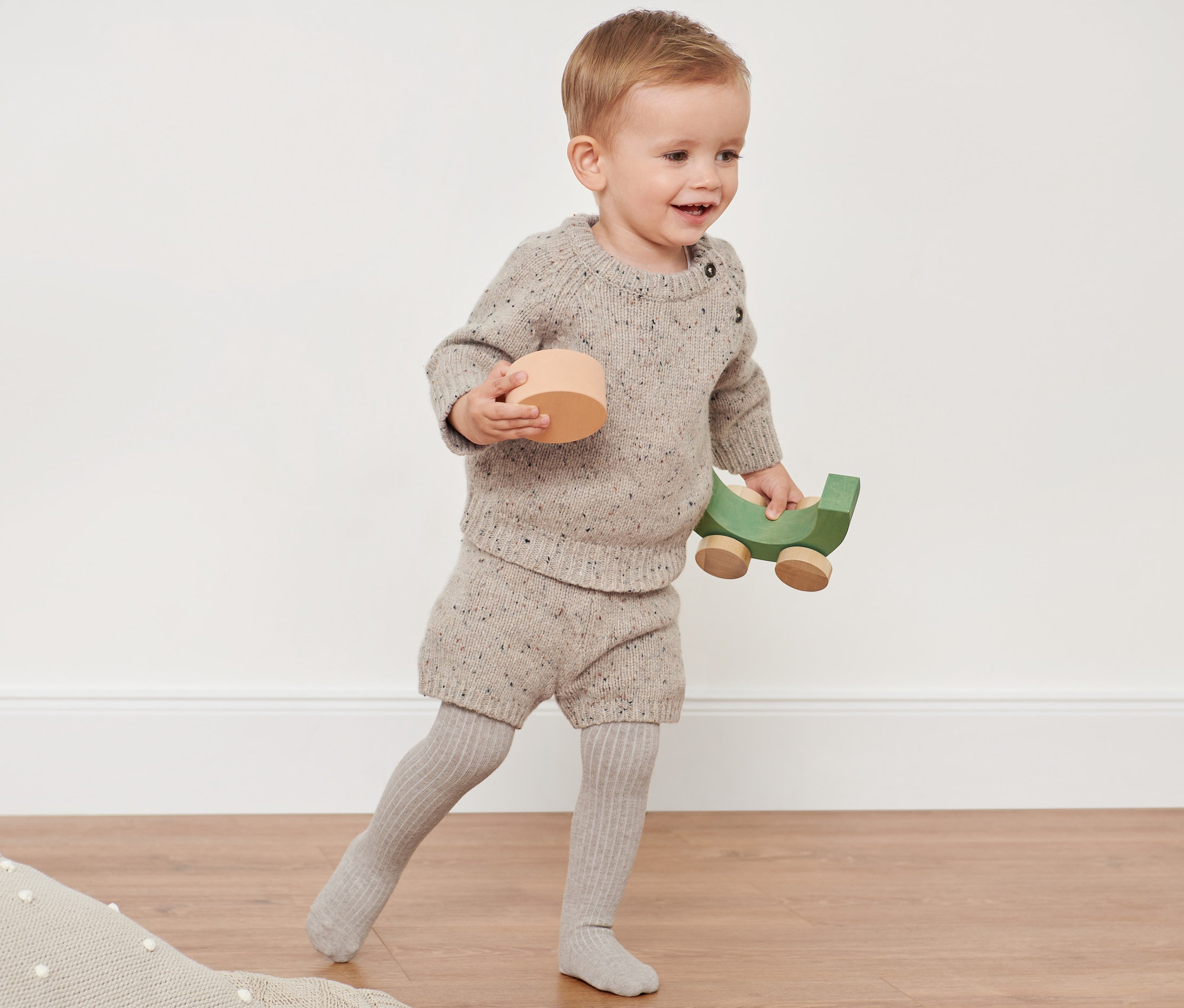 Un jeune enfant joue avec des jouets en bois et porte un ensemble en maille avec de la laine RWS.