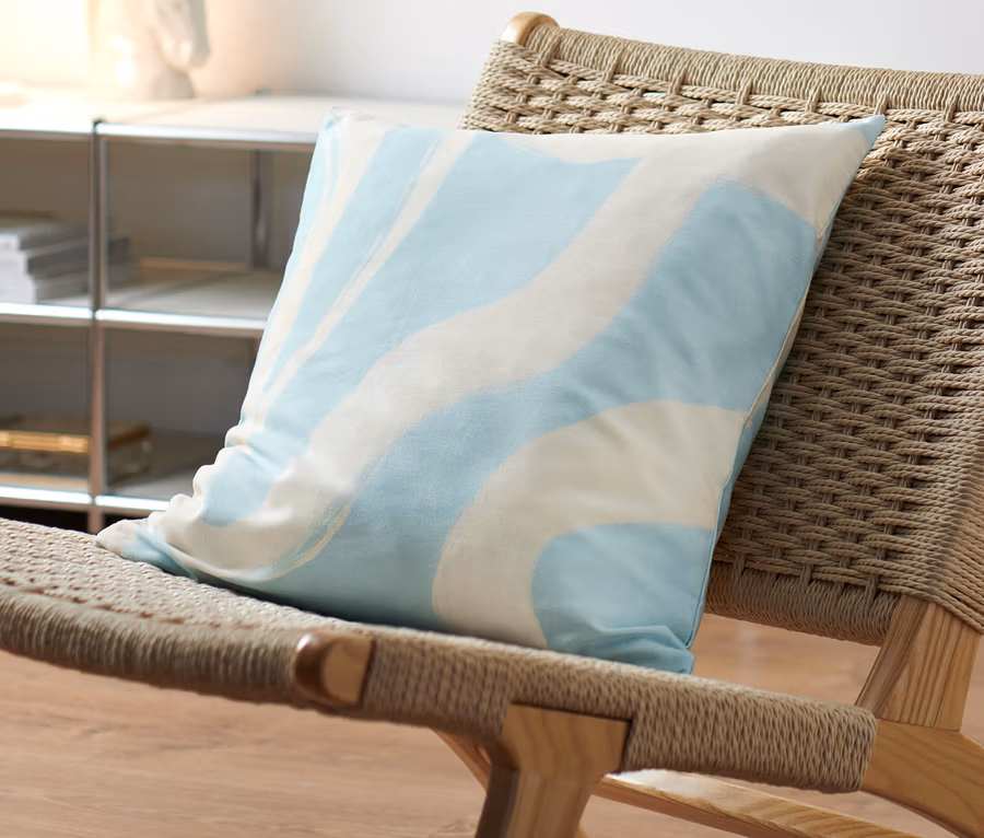 Une housse décorative pour coussin avec un motif vague sur une chaise en osier.