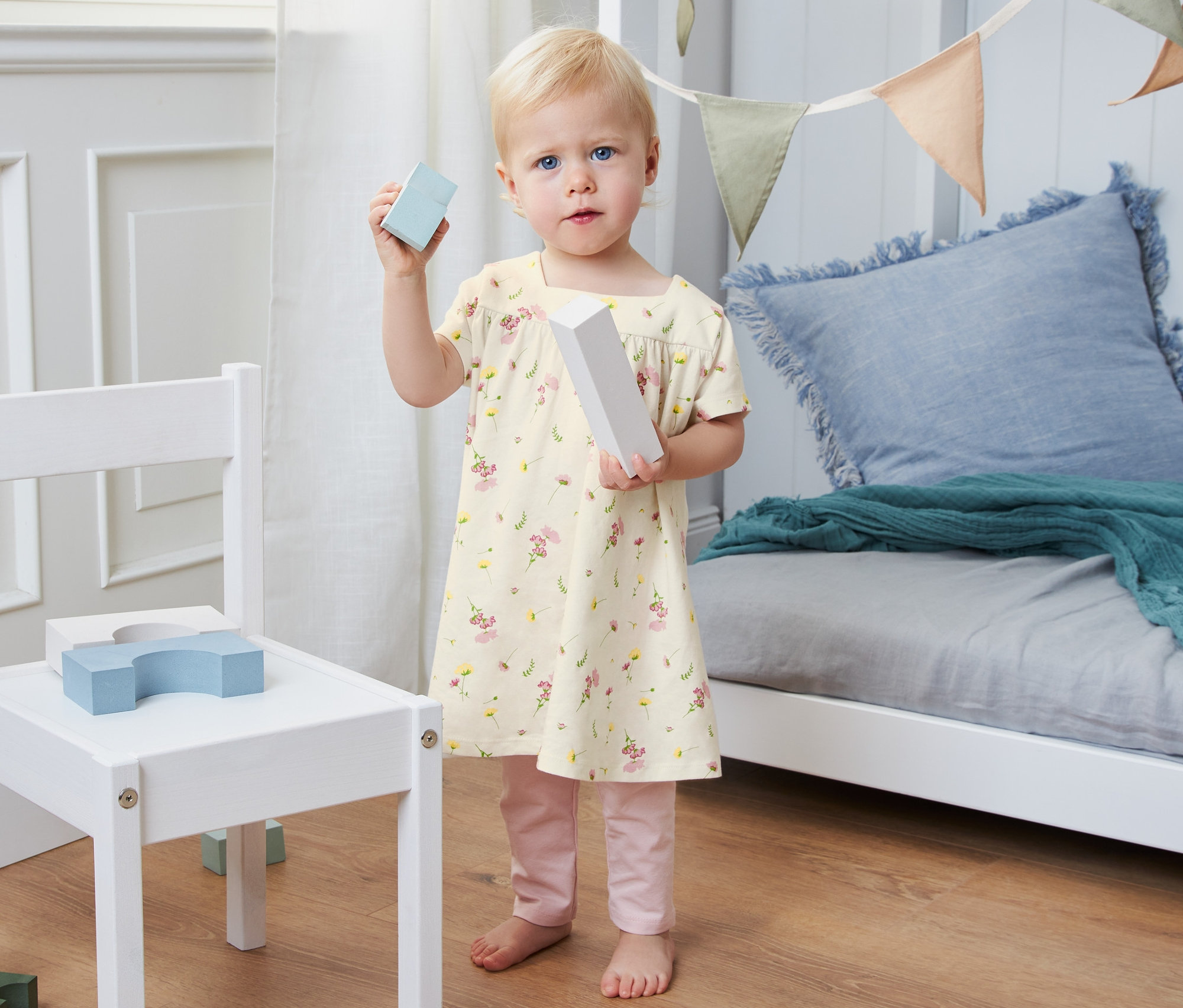 Un bébé tient des cubes dans sa main et porte une robe en jersey en coton bio.