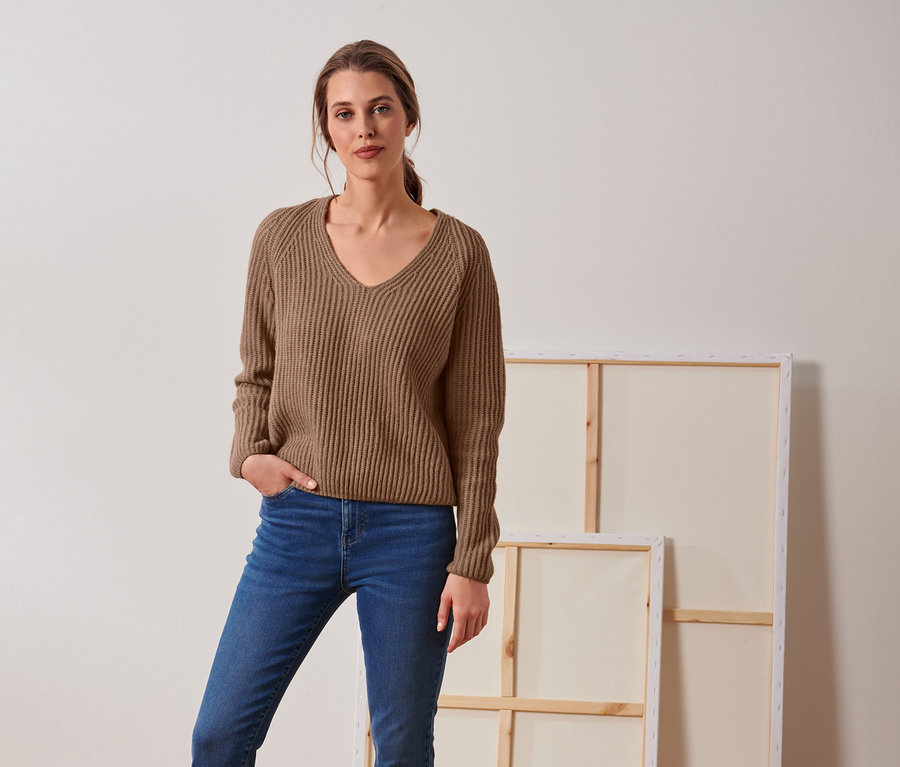 Femme posant en pull en grosse maille beige avec de la laine et un jean.