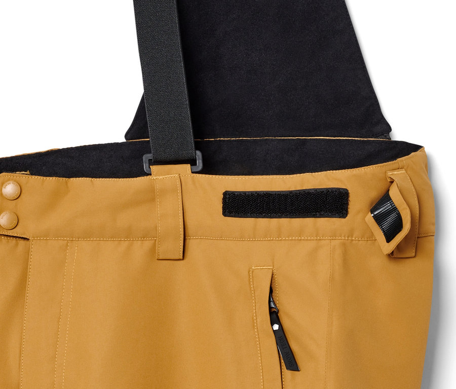 Détail d'un pantalon de ski couleur camel avec des bretelles noires.
