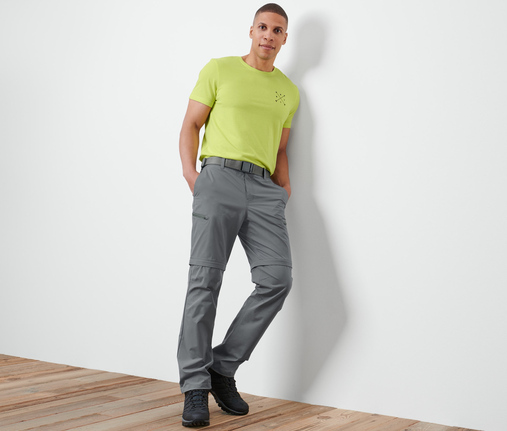 Un homme appuyé contre un mur porte un pantalon fonctionnel 2 en 1 gris.