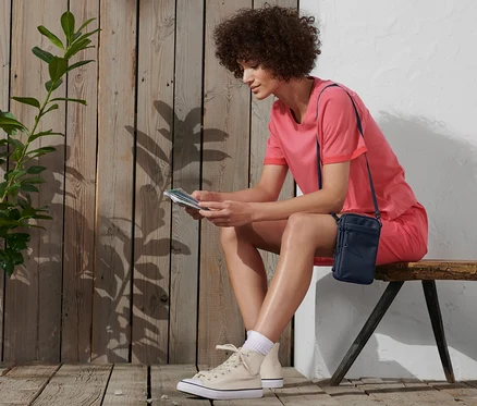 Une femme est assise sur un banc et lit. Elle porte un t-shirt et un short roses et un sac bandoulière.