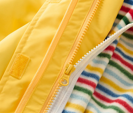Gros plan sur une veste d’extérieur 3 en 1 jaune pour enfant avec fermeture éclair et couche intérieure rayée.