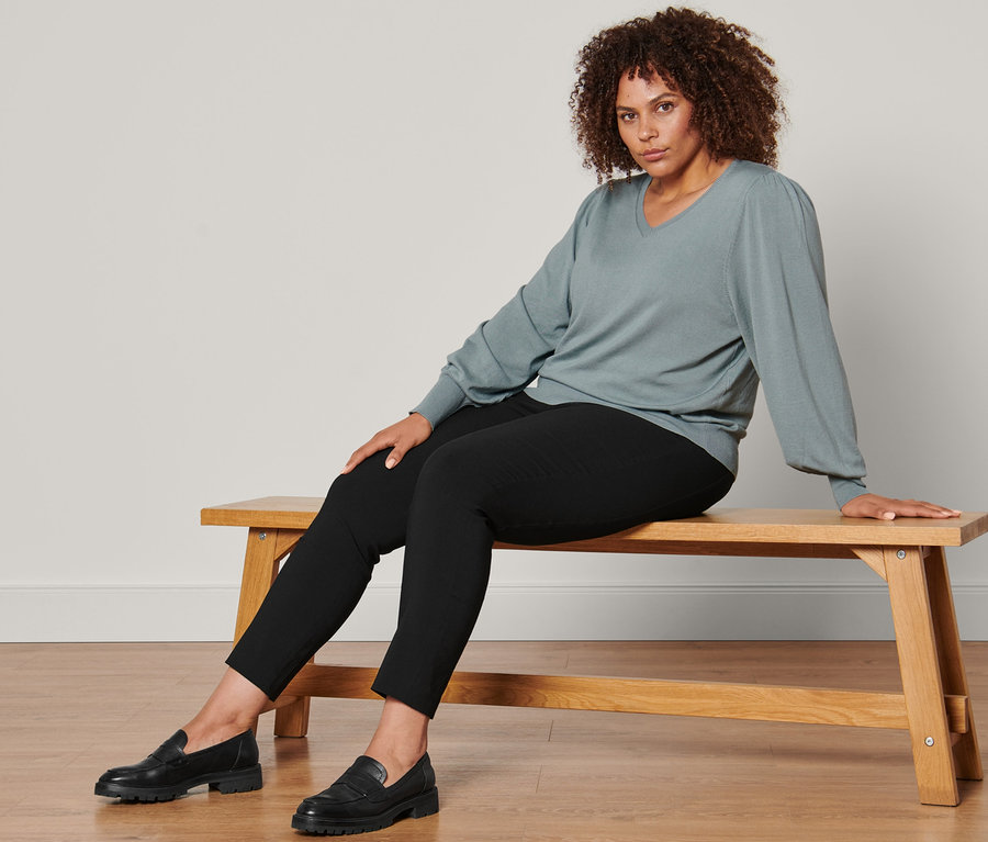 Femme assise sur un banc portant un pull en maille fine, un pantalon stretch et des mocassins en cuir.