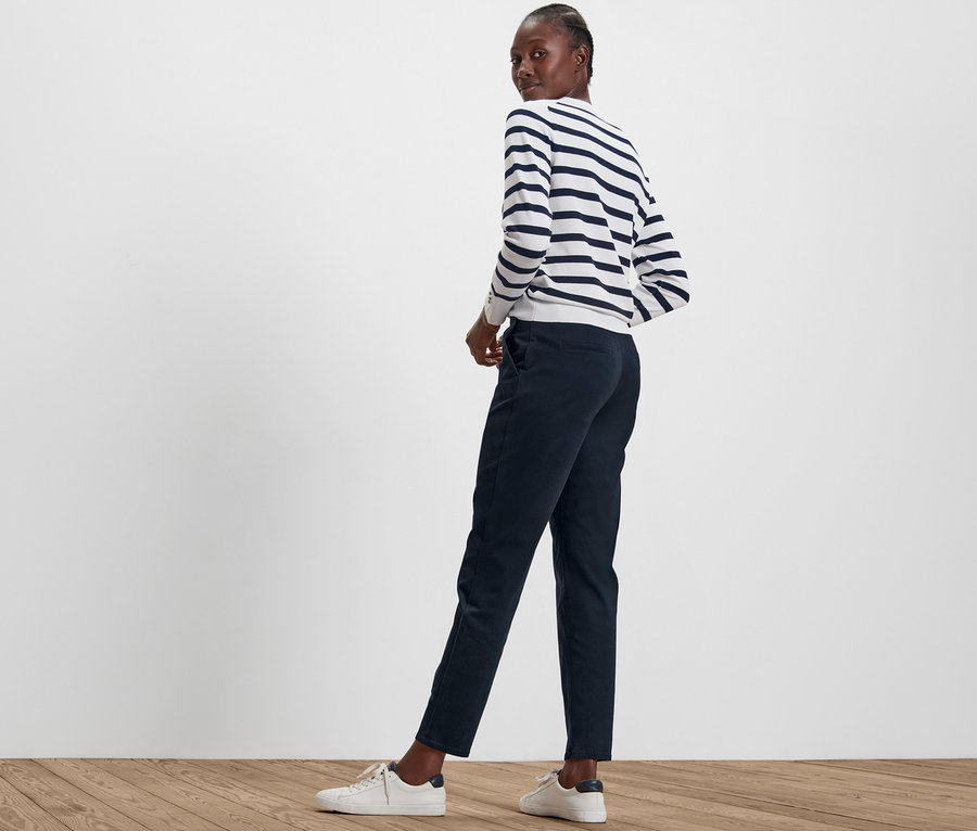 Femme regardant par-dessus son épaule portant un pantalon chino bleu marine et un haut rayé.