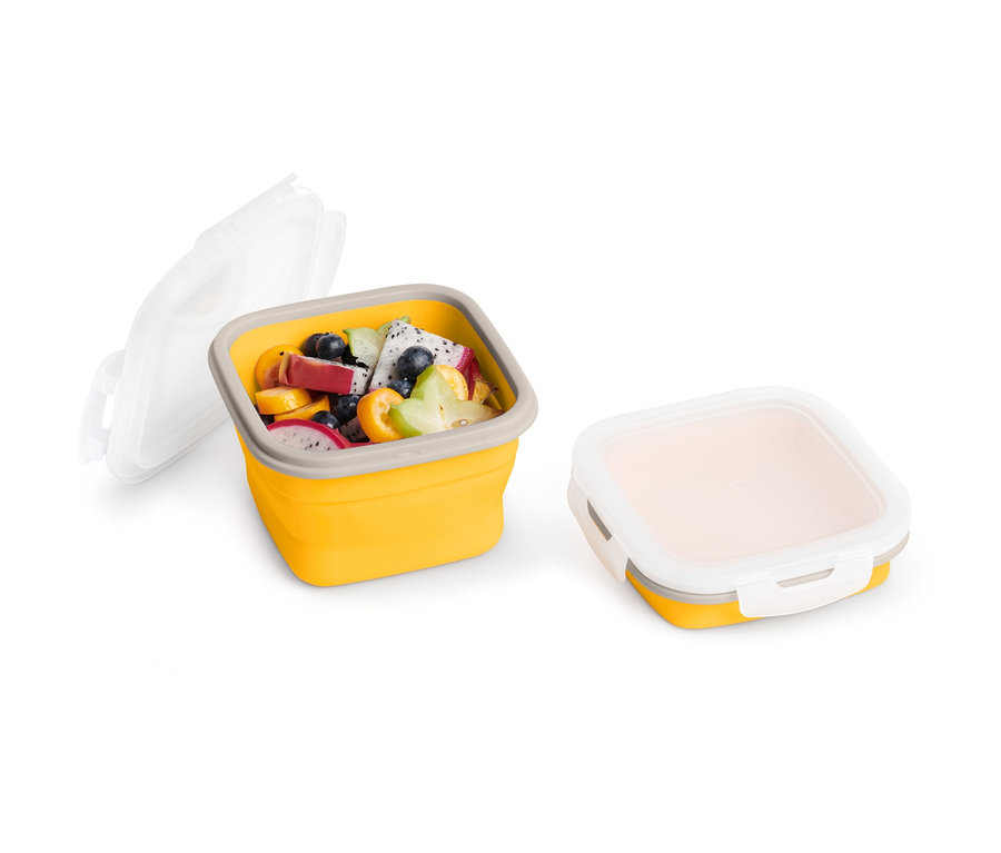Boîte fraîcheur pliable jaune ouverte avec des fruits et un couvercle à côté.