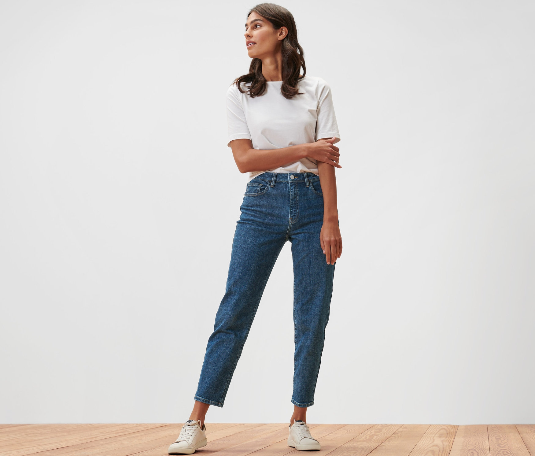 Une femme se tient sur un plancher en bois, portant un jean mom – Coupe « Nyla » et un t-shirt blanc.