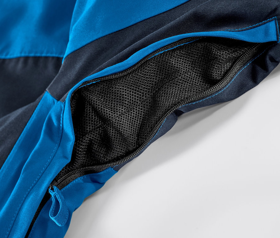 Détail d'une veste de ski bleue avec une poche zippée ouverte.