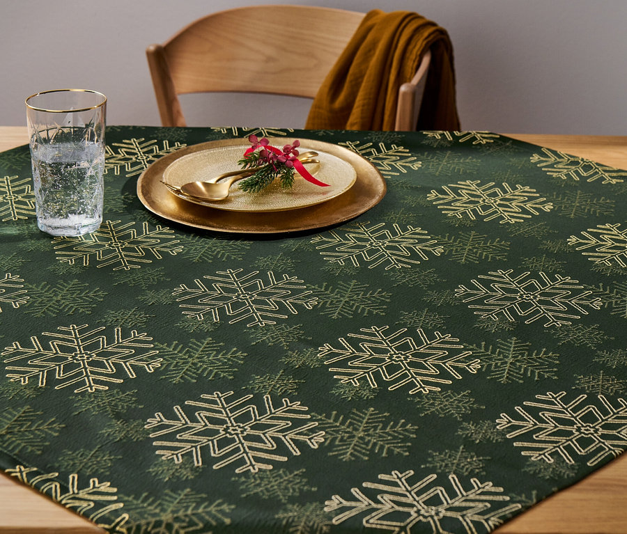 Une nappe en jacquard à motif de flocons de neige est posée sur une table, avec une assiette décorée et un verre d'eau dessus.
