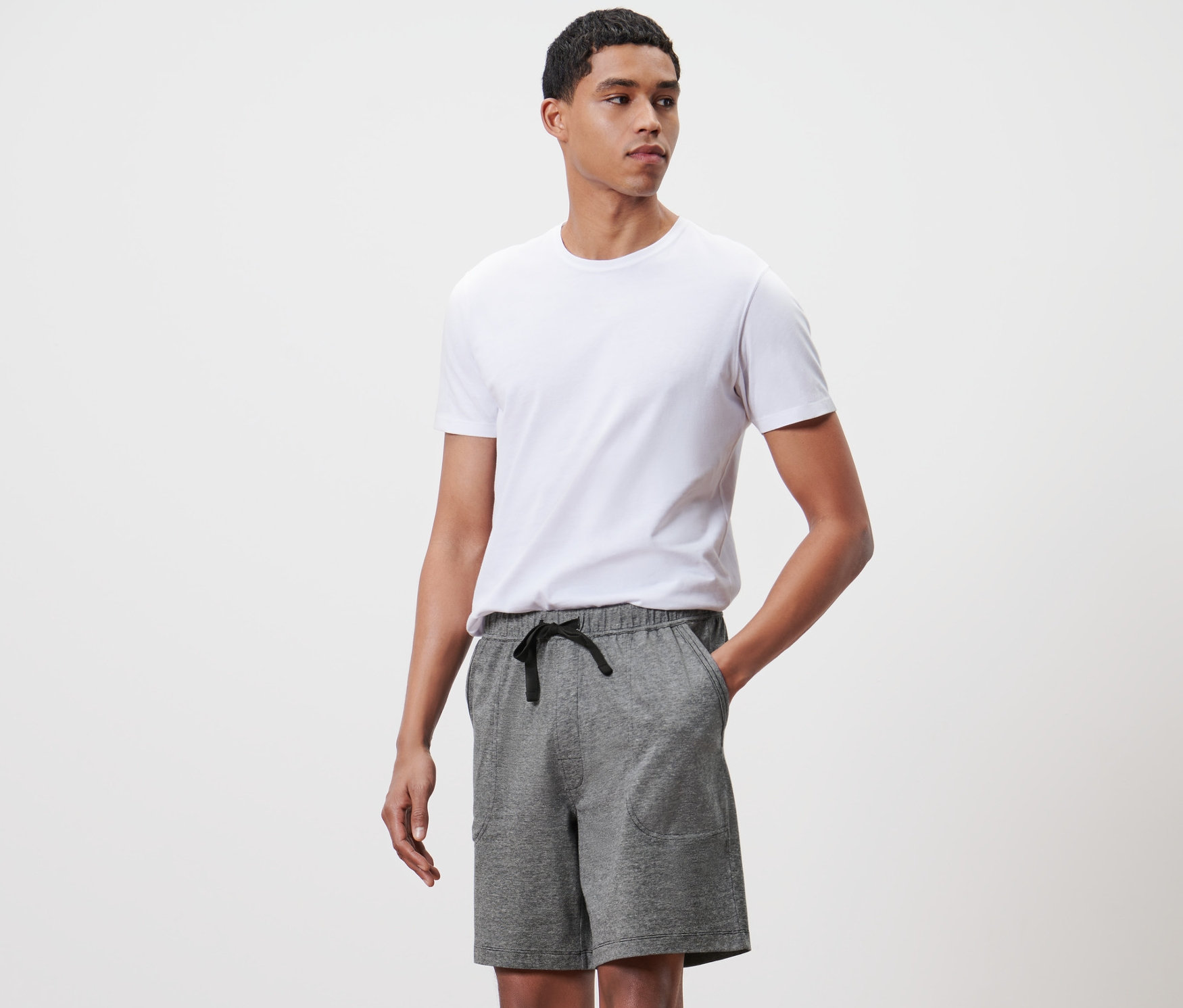Un homme debout pose en pantalon relax court gris et t-shirt blanc.