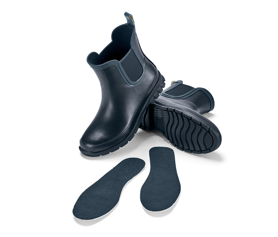 Deux Chelsea boots imperméables pour enfant et deux semelles sur fond blanc.