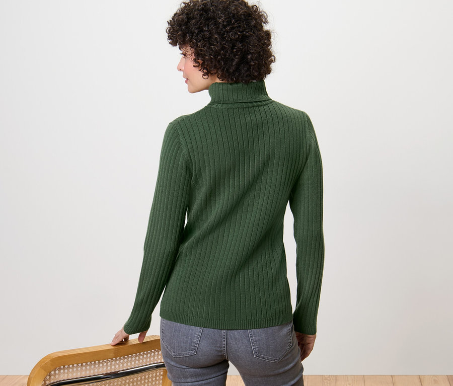 Une femme regarde par-dessus son épaule et porte un pull à col roulé côtelé vert.