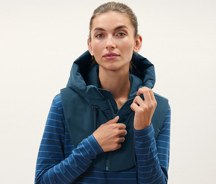 Femme ajustant une capuche matelassée avec col montant, portant un haut rayé bleu et un pantalon noir.